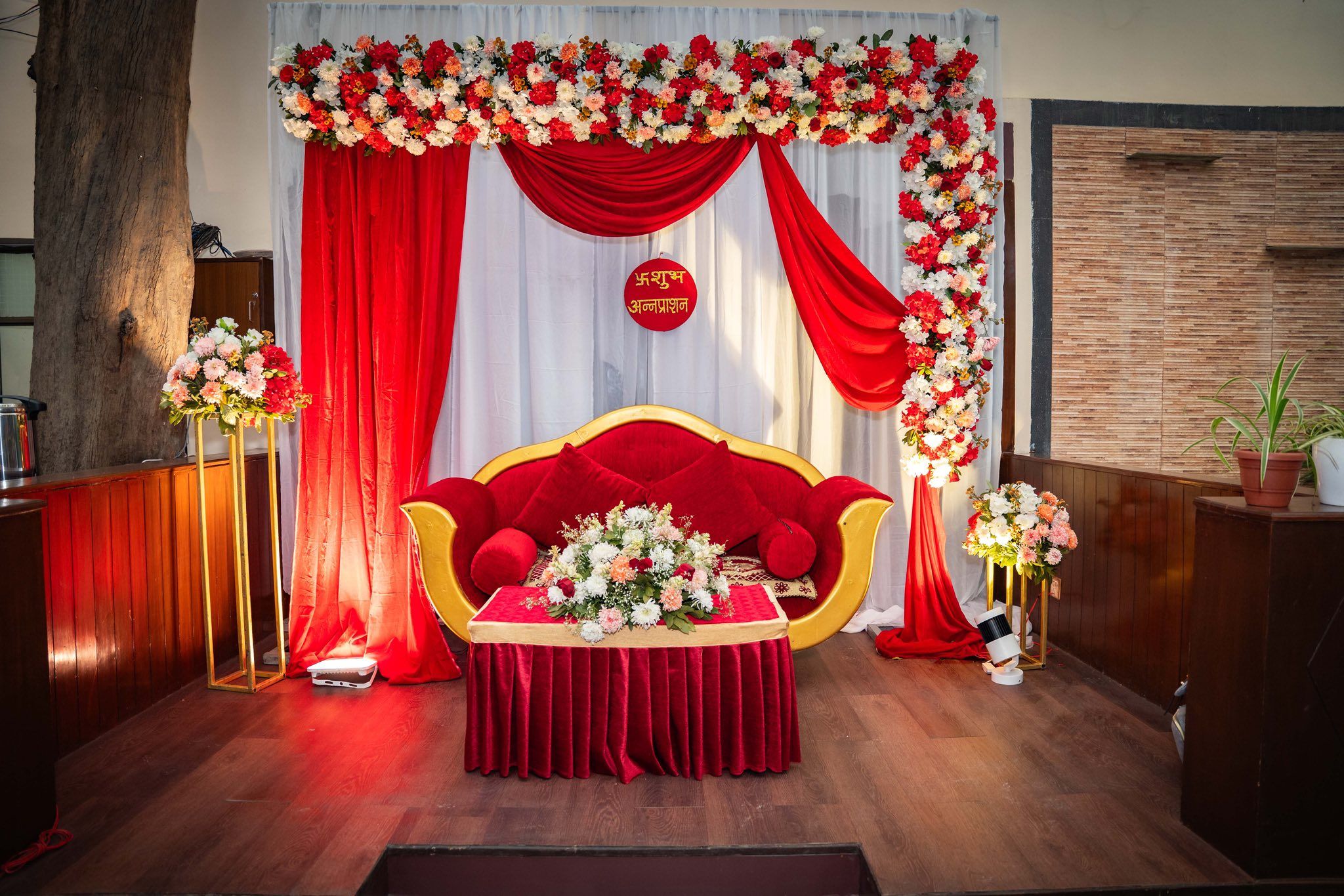 Decorated wedding stage with red drapes, a gold sofa and flower arrangements